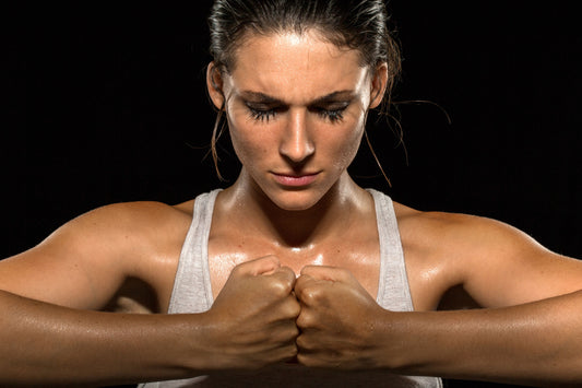 Fit woman in white tank standing with fists pressed together. Only shoulders and head are visible.